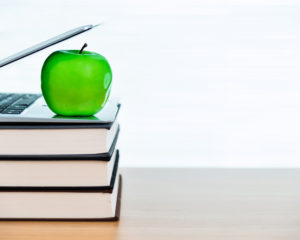 An apple on top of books and laptop